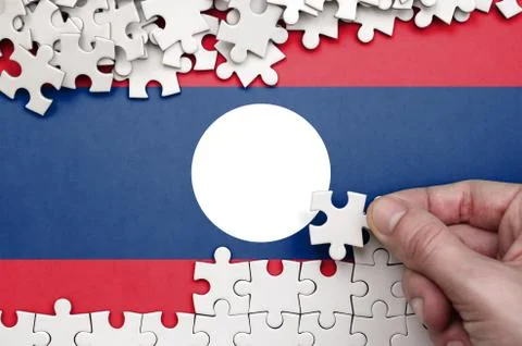 Laos flag  is depicted on a table on which the human hand folds a puzzle of w Foto stock