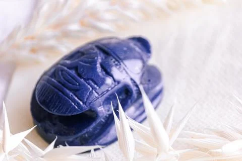 Lapis lazuli scarab beetle amulet among dried oat spikelets on linen. Stock Photos
