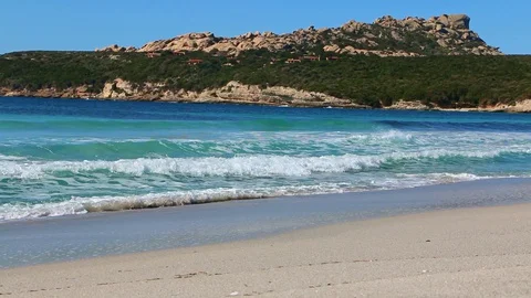 Lapping of the blue waves on the beach with cliffs behind Stock Footage 128927353