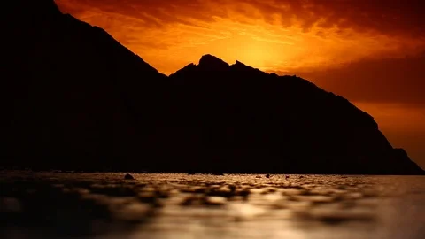 Lapping Persian Gulf, and orange sunset behind black mountain silhouettes. HD Stock Footage 89851915