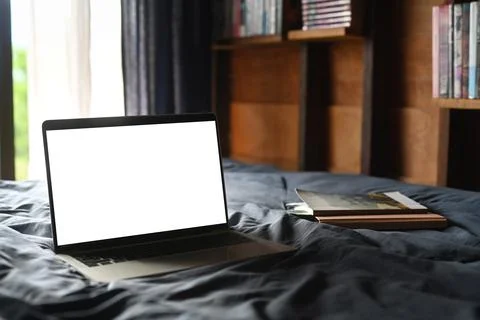 Laptop and books in comfortable bed with soft light from window. Blank screen Stock Photos