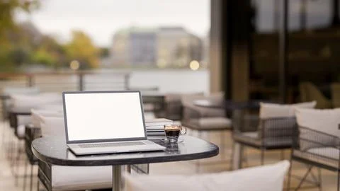 A laptop and a coffee cup on a table in the outdoor seating area of a cafe .. Stock Illustration