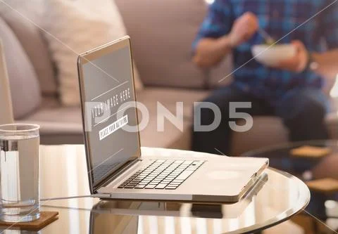 Laptop and glass of water on table Mockup PSD Template