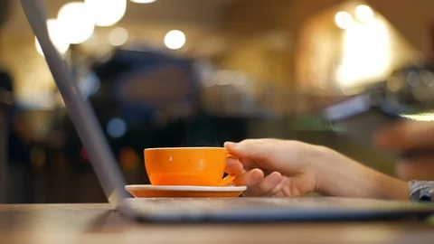Laptop and hand lifting a cup of coffee, in coffee shop, blurred background Stock-Footage 101655024