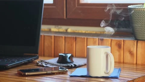 Laptop and mug of steaming coffee on a wooden table in sunlight. Stock Footage 239336495