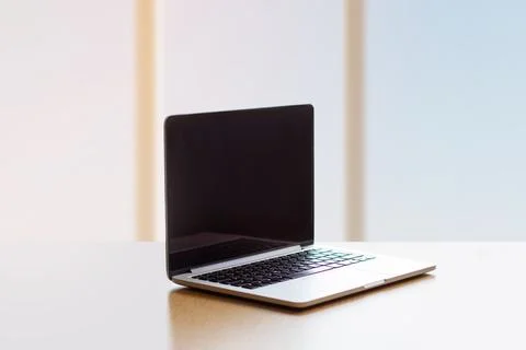Laptop with black screen on an empty table by the window, copy space, empty s Stock Photos