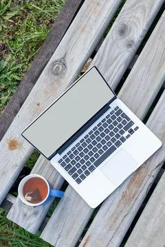 Laptop with blank screen on grey timber planks next to a hot mug of herbal te 库存照片