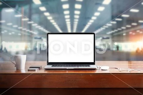 Laptop with blank screen on table and workspace in office background ...