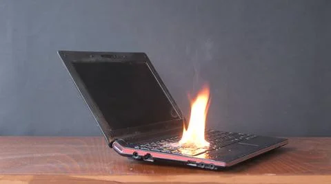 The laptop caught fire on the table, flames and sparks, ignition of the battery  Stock Photos