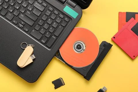 Laptop with CD disk and different memory storage devices on yellow background Stock Photos