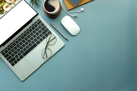 Laptop computer with blank display, earphone, coffee cup and notebook on blue Foto stock
