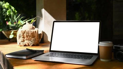 Laptop computer with blank screen, coffee cup and notebook on wooden table at Stock Photos