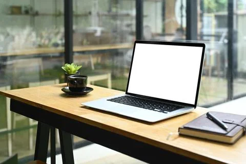 A laptop computer with blank screen, coffee cup and notebook on wooden table in Stock Photos