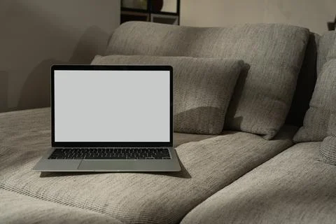 Laptop computer with blank screen on comfortable sofa in sunlight shadows. Mi Stock Photos