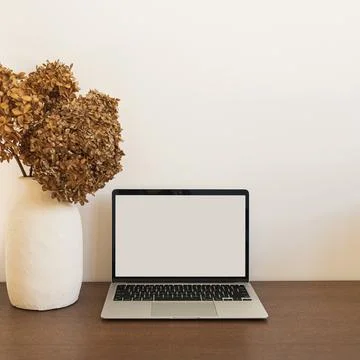 Laptop computer with blank screen. Dried hydrangea flower bouquet on wooden t Stock Photos