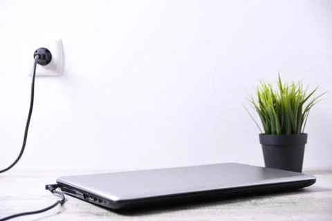 Laptop, computer is charging from a 220-volt outlet on a desk near the wall.  Stock Photos