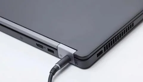 Laptop computer with charging cable plugged in on a white surface Stock Photos