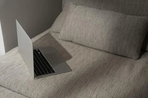 Laptop computer on comfortable sofa in sunlight shadows. Minimal modern style Stock Photos
