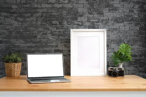 Laptop computer, empty picture frame, camera and houseplant on wooden table w Stock-Fotos