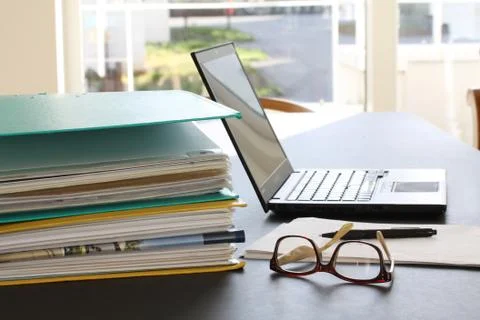 Laptop computer, glasses, paper sheets and ring binders filled with papers Stock Photos