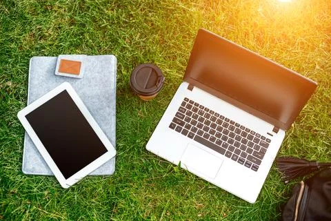 Laptop computer on green grass with coffee cup, bag and tablet in outdoor par Stock Photos