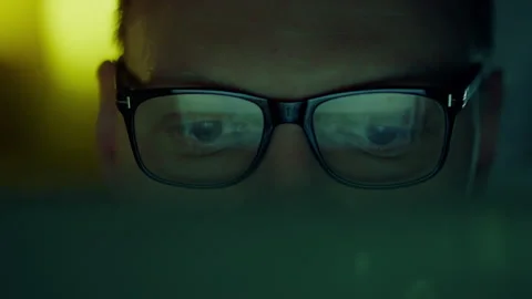 A laptop computer illuminates the face of a bespectacled programmer, who is Stock-Footage 263902873