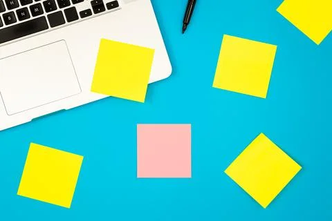 Laptop computer with many sticky notes on a blue background, flat lay. Stock Photos