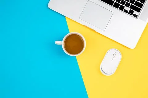 Laptop, computer mouse and cup of coffee on a yellow and blue background. Stock Photos