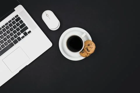 Laptop, computer mouse, a cup of coffee and cookies on a black background. Stock-Fotos