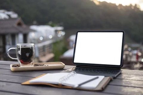 Laptop computer, notebook and coffee cup on wooden table with blurred mountai Stock Photos