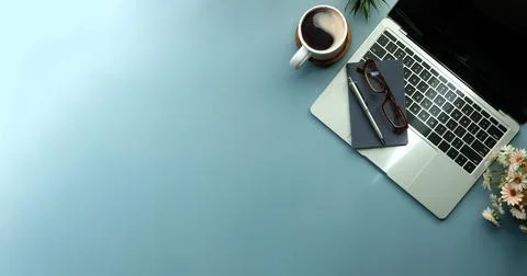 Laptop computer, notebook and cup of hot coffee on blue background. Stock Photos