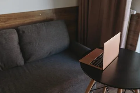 Laptop computer on side table near comfortable sofa. Minimalist aesthetic wor Stock Photos