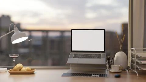 A laptop on a computer stand and accessories on a wooden desk against the w.. Ilustración de archivo