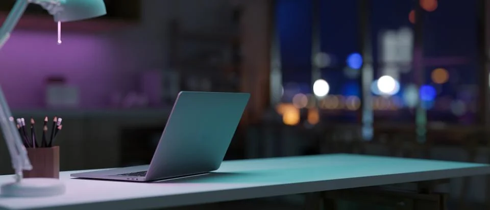 A laptop computer on a table in a modern dark office room at night features.. イラスト素材