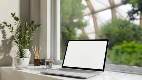 A laptop computer white-screen mockup on a white table against the window w.. Illustrazione stock