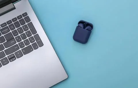 Laptop computer with wireless earbuds on blue background Stockfoto's