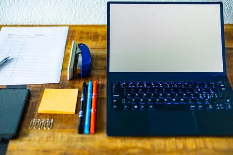 A laptop is on a desk with a stack of papers and a pen Stock Photos