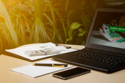 Laptop with dollars and telephone on the table on the background of plants Stock Photos