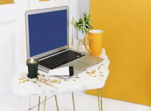 Laptop with empty blue screen and yellow mug placed on small table with candle 写真素材