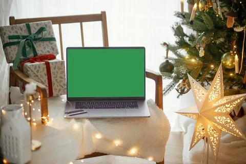 Laptop with empty screen and stylish christmas gifts on modern chair on bac.. Stock Photos