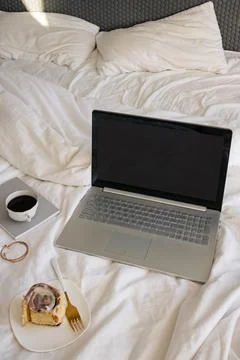 Laptop with empty screen on the bed with cinnamon bun and burning candle Stock Photos