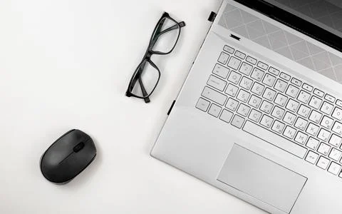 A laptop with glasses and computer mouse are on a white table. Top view with Stock Photos