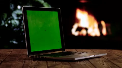 Laptop with a green screen chroma key screen against a cozy fireplace and Stock Footage 320586013