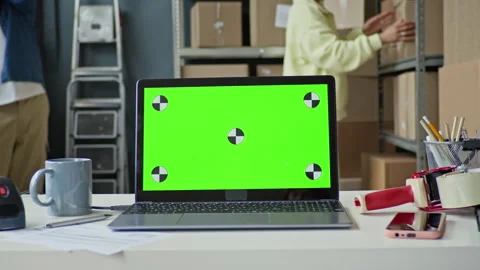 Laptop with Green Screen on Desk with Workers Packaging Boxes in Background Stock Footage 337308745