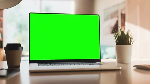 A laptop with a green screen sits on a table in a bright home office. The c.. 스톡 동영상 278665751
