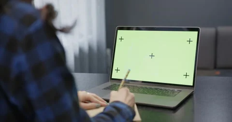 A laptop with a green screen is on the table, in front of the girl. Stock Footage 188712131