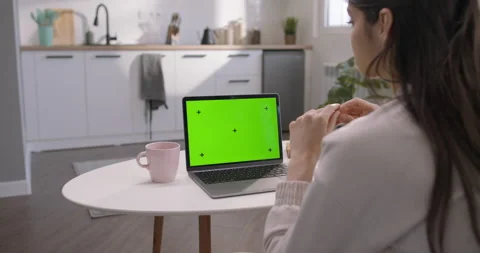 Laptop with green screen on white table in kitchen next to coffee mug. Woman 動画素材 236970648