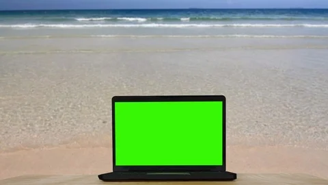 Laptop with green screen on wooden table, beautiful beach background. Stock Footage