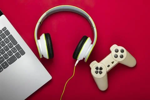 Laptop with headphones and game controller on red background Stock Photos