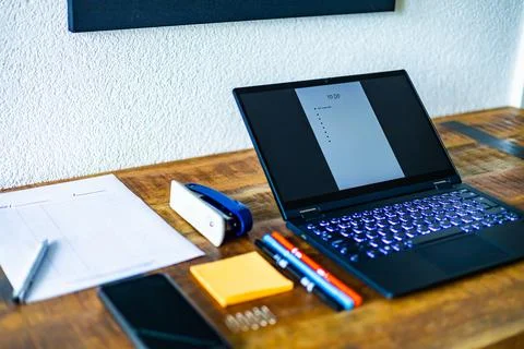 A laptop is open on a desk with a stack of papers and a pen Stock Photos